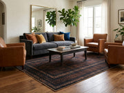 7' x 10' Rectangular Black Rust Brown Distressed Geometric Tribal Traditional Area Rug styled in a living room with a dark gray sofa and wooden coffee table.