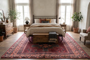 7' x 10' Rectangular Burgundy & Black Geometric Tribal Southwestern Area Rug placed beneath a bed with cream bedding and a wooden bench.