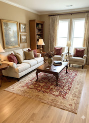 7' x 10' beige and red traditional floral area rug placed under a wooden coffee table in a classic living room with neutral seating and warm decor.