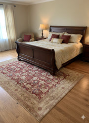 7' x 10' beige and red traditional floral area rug styled partially under a wooden bed in a traditional bedroom with cream bedding and warm lighting.