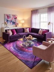 7' x 10' purple and pink abstract modern rectangular area rug placed in a stylish living room with a deep purple sectional sofa, glass coffee table, and pastel decor accents.