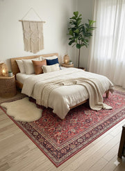 7' x 10' red, beige, and soft brown floral medallion traditional area rug positioned partially under a bed in a warm, neutral bedroom with woven textures.