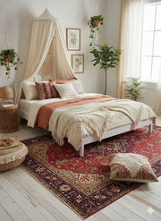7' x 10' red, navy, and cream traditional Persian-style area rug placed under a bed in a bright boho-inspired bedroom with neutral bedding and hanging plants.