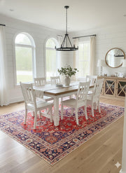 7' x 10' red, navy blue, and cream floral medallion traditional area rug placed under a dining table in a bright dining area with white chairs.