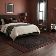 7' x 7' Square Black & Burgundy Minimalist Linear Geometric Modern Washable Area Rug placed in a bedroom beneath a charcoal upholstered bed with white bedding.