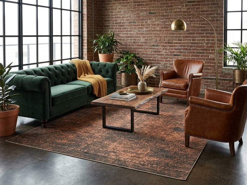 7' x 7' Square Dark Brown & Rust Distressed Abstract Modern Washable Area Rug styled in an industrial living room with a green velvet sofa, brown leather armchairs, and wooden coffee table.