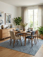 7' x 7' Square Light Blue & Navy Blue Wavy Striped Abstract Modern Washable Area Rug styled in a dining room with a round wooden dining table and upholstered chairs.