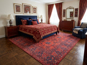 7' x 7' Square Red & Navy Tribal Geometric Traditional Area Rug placed beneath a bed with red patterned bedding and a navy upholstered headboard.