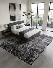 7' x 9' Rectangular Charcoal Gray Ivory Distressed Abstract Modern Washable Area Rug placed in a bedroom with a gray upholstered bed and white bedding.