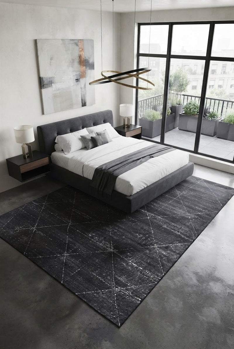 7' x 9' Rectangular Charcoal Gray Ivory Distressed Diamond Geometric Modern Washable Area Rug placed in a bedroom with a gray upholstered bed and white bedding.