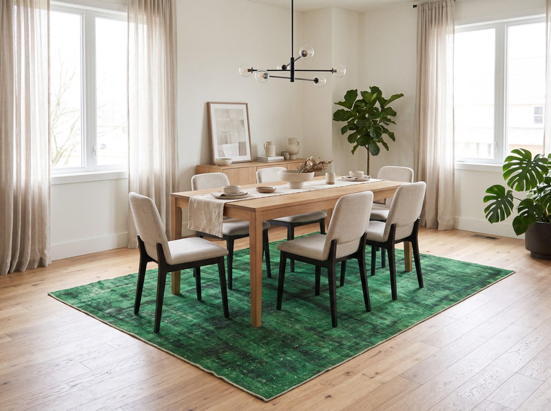 7' x 9' Rectangular Emerald Green & Black Distressed Abstract Modern Washable Area Rug styled in a dining room beneath a wooden dining table and cream upholstered chairs.