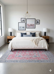 7' x 9' Rectangular Pink & Blue Gray Ivory Distressed Traditional Area Rug placed / styled in a contemporary bedroom beneath a neutral upholstered bed with wooden nightstands.