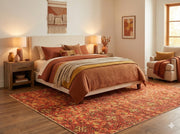 7' x 9' Terracotta Ivory Beige Vintage Tribal Area Rug placed / styled in a warm neutral bedroom beneath a light upholstered bed with rust and mustard bedding, wood nightstands, and soft ambient lighting.
