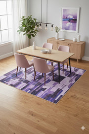 7' x 9' lavender, purple, and black geometric modern area rug placed beneath a light wood dining table with blush upholstered chairs.