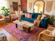7' x 9' raspberry pink multi-color washable bohemian medallion area rug placed in a vibrant bohemian living room with a teal sofa, woven chairs, and layered textured décor.