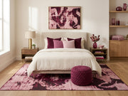 8' x 10' Blush Pink Burgundy Distressed Abstract Modern Washable Area Rug placed in a bedroom with a cream bed, burgundy pillows, and matching ottoman.