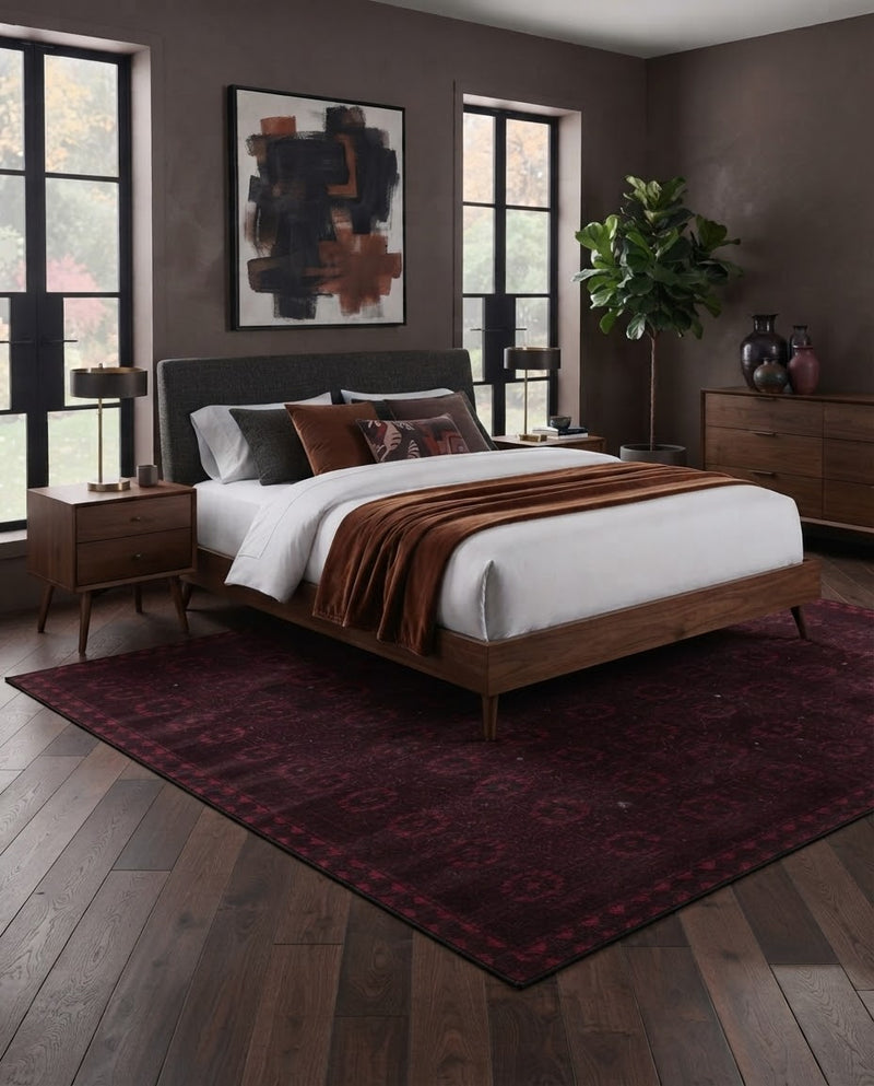 8' x 10' Rectangular Black Burgundy Geometric Tribal Traditional Washable Area Rug placed in a contemporary bedroom with a dark upholstered bed, white bedding, rust-colored accent pillows, wooden nightstands, and black-framed windows