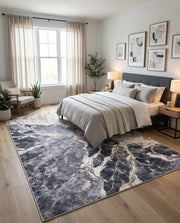 8' x 10' Rectangular Charcoal Gray Ivory Gold Marble Abstract Modern Washable Area Rug placed in a bedroom with a gray upholstered bed and white bedding.