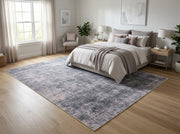 8' x 10' Rectangular Charcoal Gray Light Gray Distressed Abstract Modern Washable Area Rug placed in a bedroom with a gray upholstered bed and white bedding.