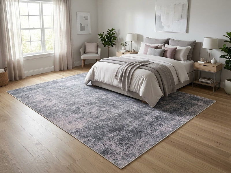 8' x 10' Rectangular Charcoal Gray Light Gray Distressed Abstract Modern Washable Area Rug placed in a bedroom with a gray upholstered bed and white bedding.