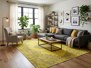 8' x 10' Rectangular Mustard Gold Gray Distressed Floral Medallion Traditional Washable Area Rug styled in a living room with a charcoal gray sofa, beige accent chair, and wooden coffee table.