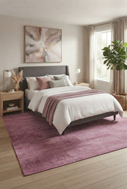 8' x 12' Rectangular Dusty Pink Mauve Solid Textured Modern Washable Area Rug placed in a modern bedroom with a gray upholstered bed and soft pink accents.