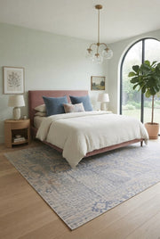 8' x 12' Rectangular Ivory Light Blue Distressed Tribal Vintage Washable Area Rug placed in a cozy bedroom with a pink upholstered bed and neutral decor.