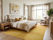 8' x 12' Rectangular Mustard Yellow Gold Ombre Modern Washable Area Rug placed in a cozy bedroom with a wooden bed, cream bedding, and mustard accent pillows.