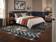 8' x 12' Rectangular Navy Blue Red Stars and Stripes Patriotic Americana Area Rug placed in a cozy bedroom with a navy upholstered bed, white bedding, rust-colored throw blanket, and wooden furniture.