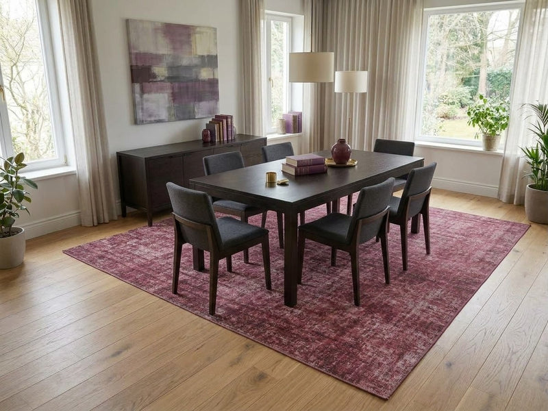 8' x 12' Rectangular Rose Pink Burgundy Distressed Abstract Vintage Area Rug styled in a modern dining room with a dark wooden dining table, gray upholstered chairs, abstract wall art, and floor-to-ceiling curtains.