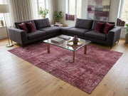 8' x 12' Rectangular Rose Pink Burgundy Distressed Abstract Vintage Area Rug styled in a modern living room with a charcoal gray sectional sofa, burgundy accent pillows, glass coffee table, and large windows.