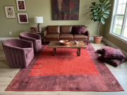 8' x 12' Rectangular Rust Red Burgundy Solid Border Modern Contemporary Area Rug styled in a cozy living room with a brown leather sofa, burgundy velvet accent chairs, wooden coffee table, and olive green walls.