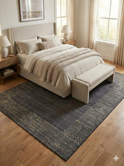8' x 12' charcoal and warm taupe distressed modern washable area rug styled beneath a bed in a calm bedroom with neutral bedding, wood nightstands, and soft natural lighting.