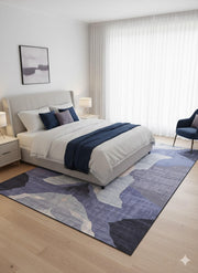 8' x 12' purple gray abstract washable area rug placed under a bed in a modern bedroom with neutral bedding and soft lighting.